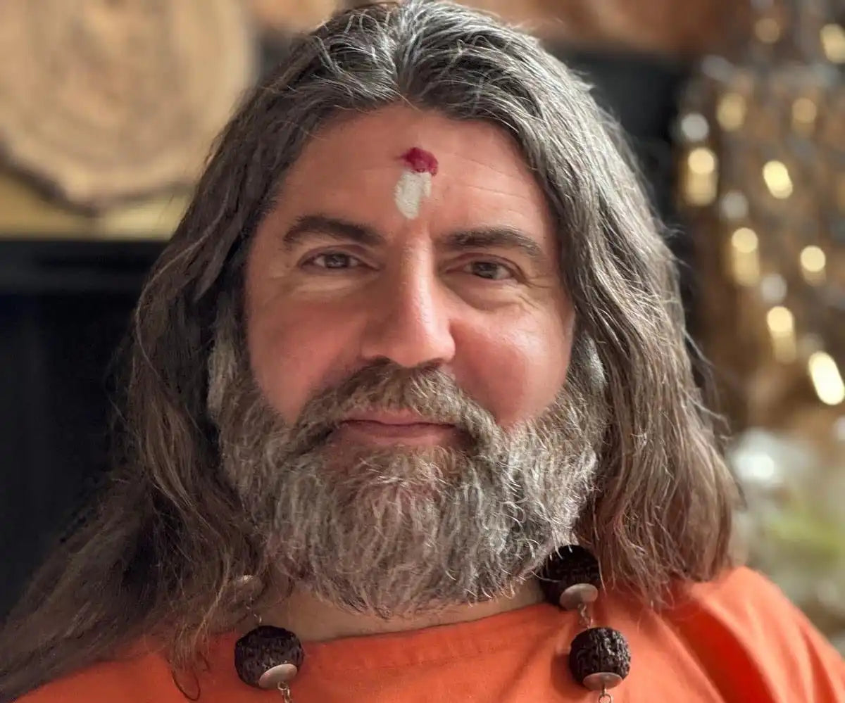 A bearded person wearing an orange garment and traditional Hindu tilak marking on their forehead.