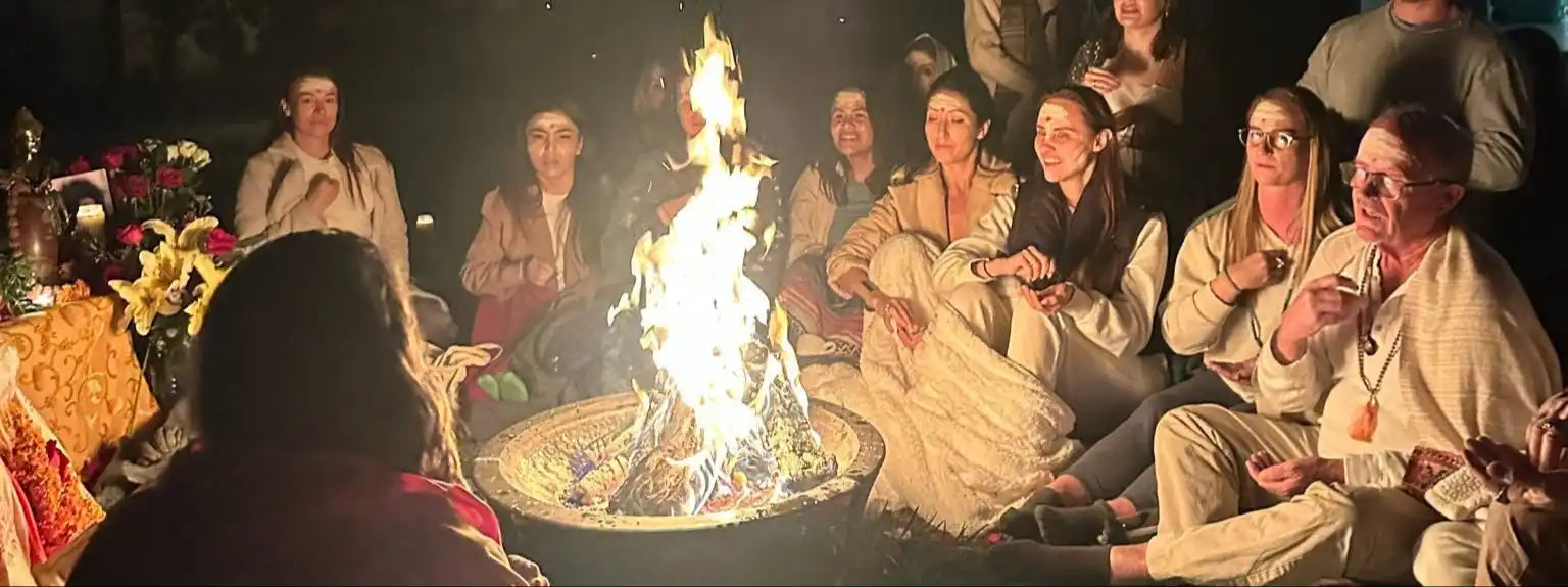 Bright fire burning in a metal fire pit with people gathered around it.