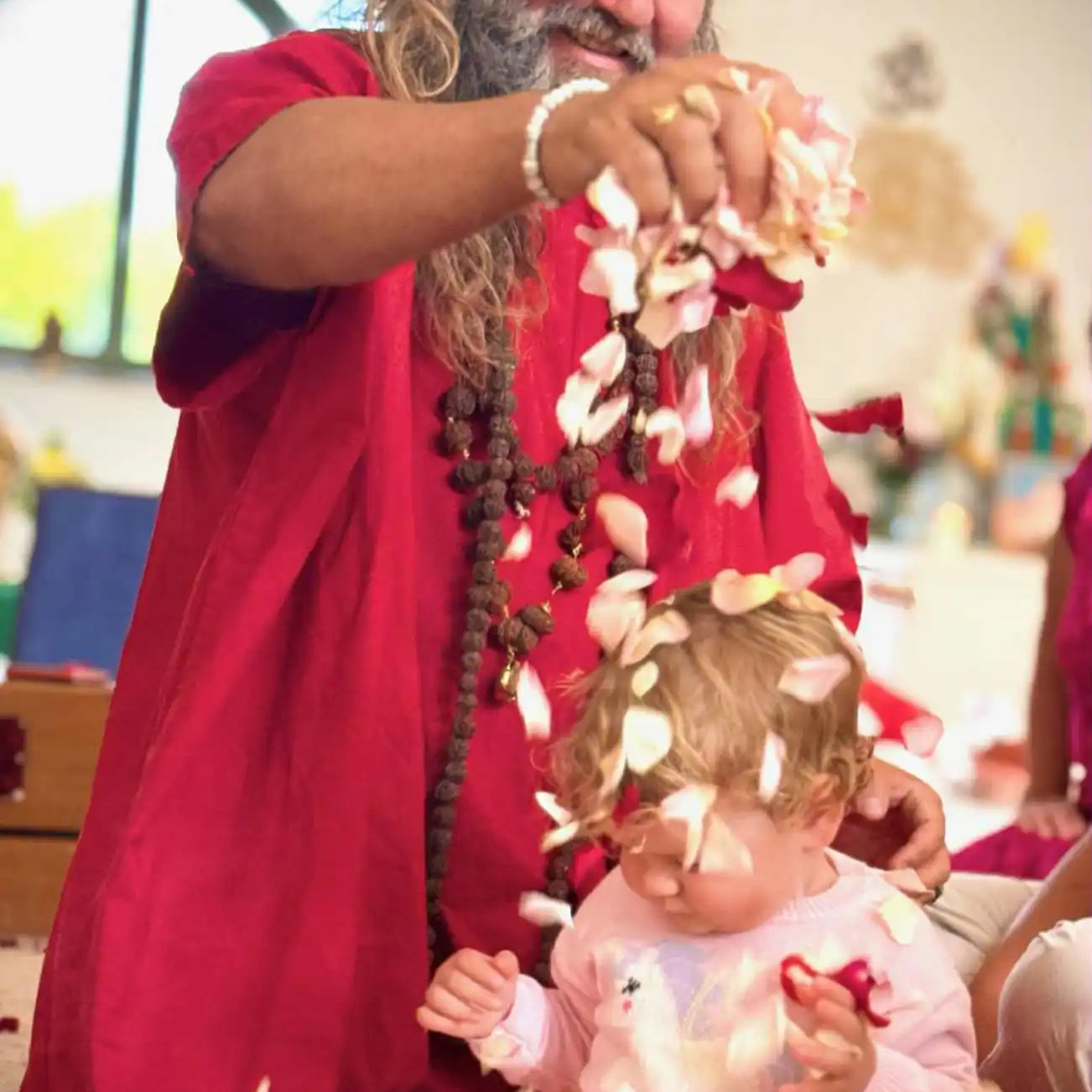 A man in traditional Indian attire showering a child with rose petals.