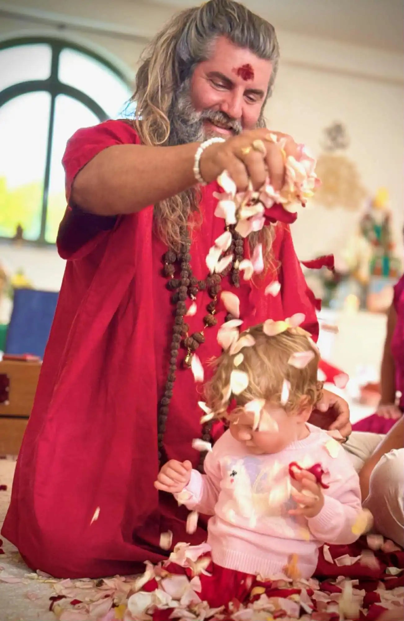 A man in traditional Indian attire showering a child with rose petals.