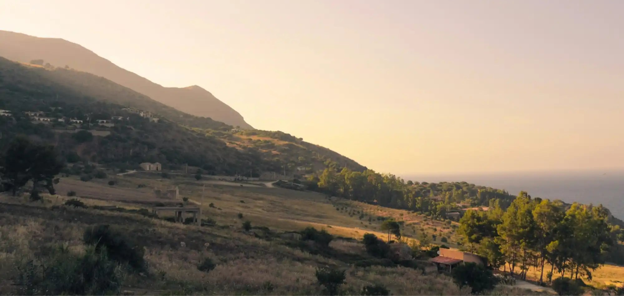 Mountainous coastal landscape at sunset with rolling hills descending toward the sea.