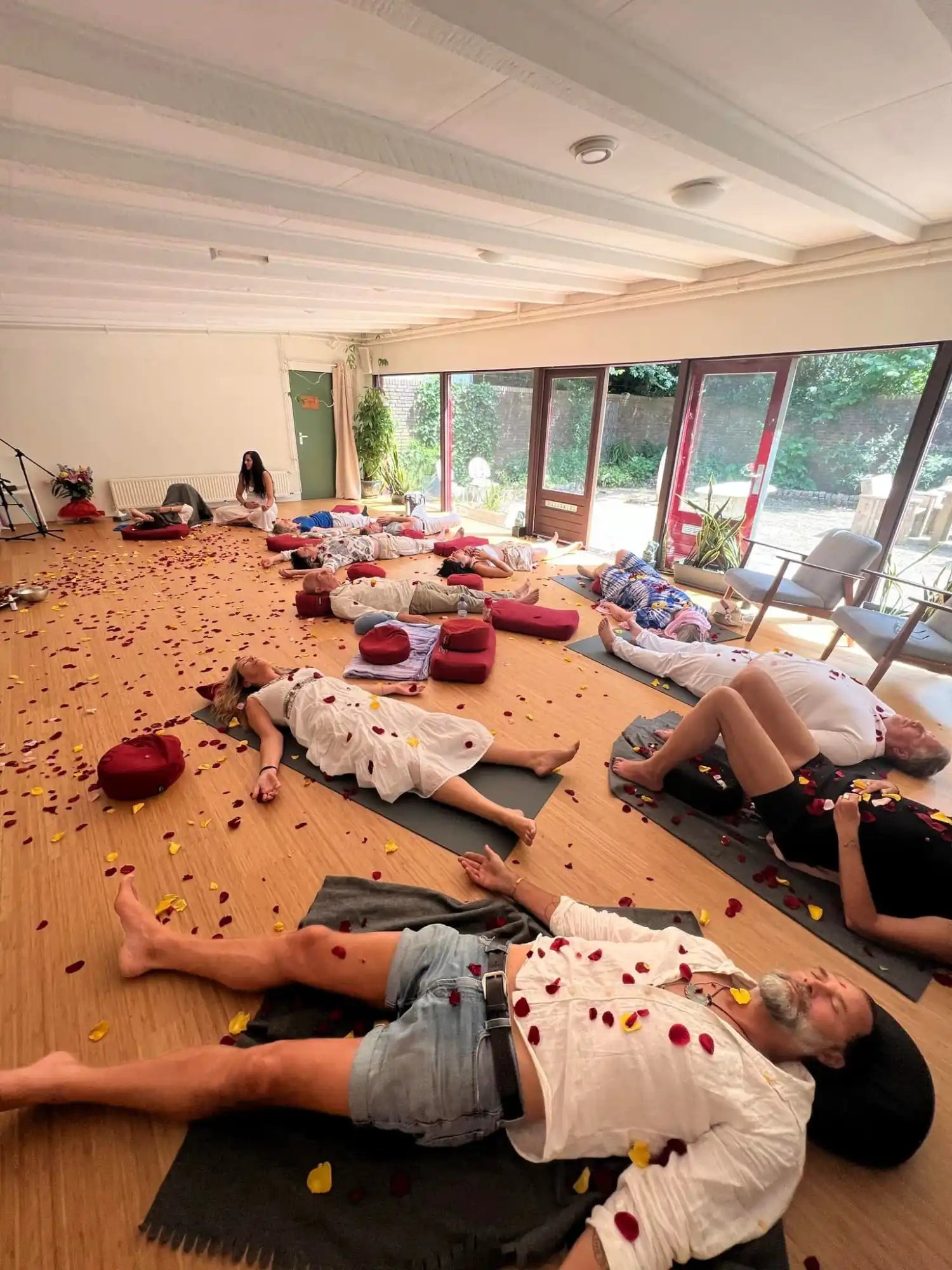 Several people lying on yoga mats in a relaxation pose with rose petals scattered around them.
