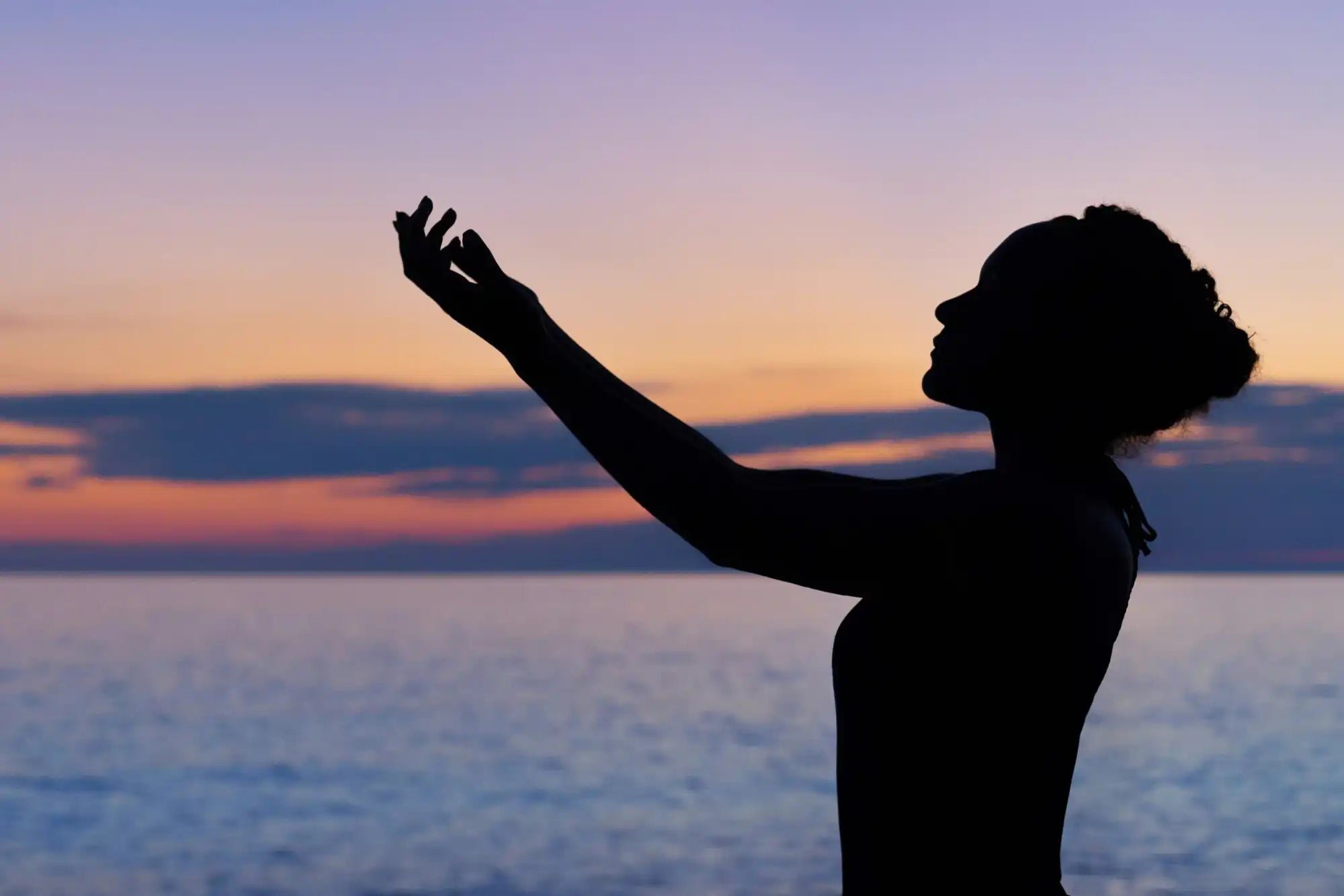 A silhouetted figure reaching upward against a sunset sky.