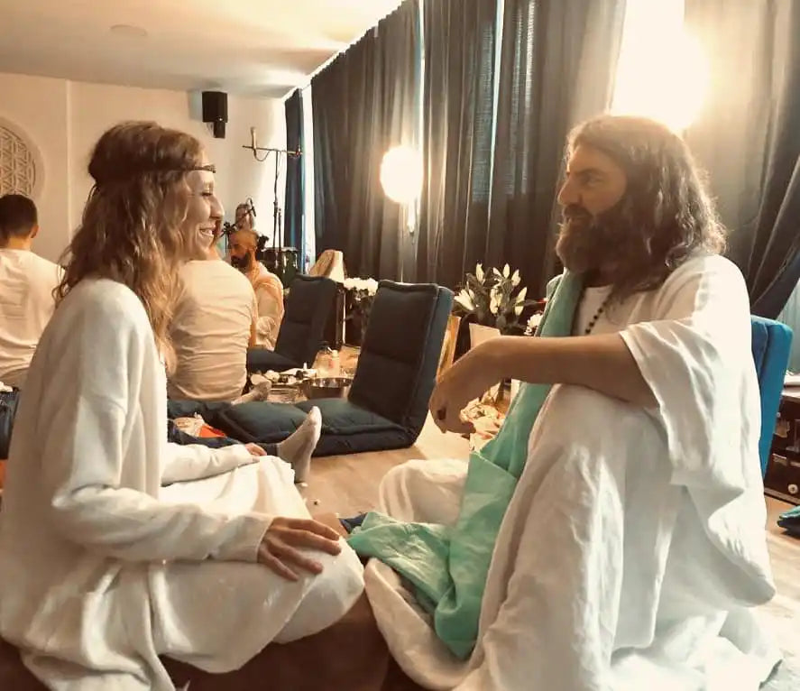 Two people in white clothing having a conversation while seated.