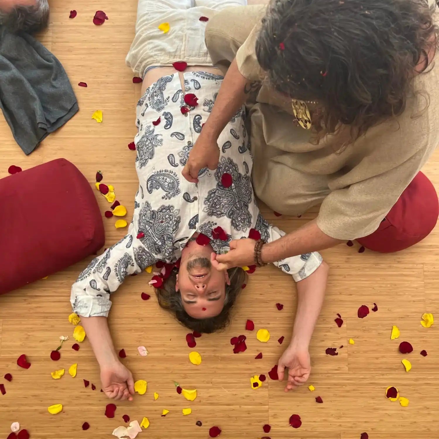 Two people lying on a wooden floor surrounded by scattered rose petals.