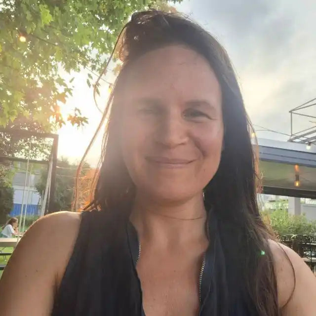 A woman with long dark hair smiling outdoors at sunset.