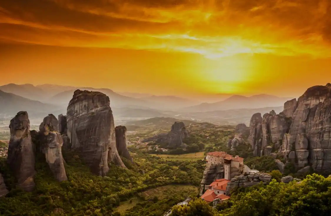 Ancient monasteries perched on towering rock formations at sunset.