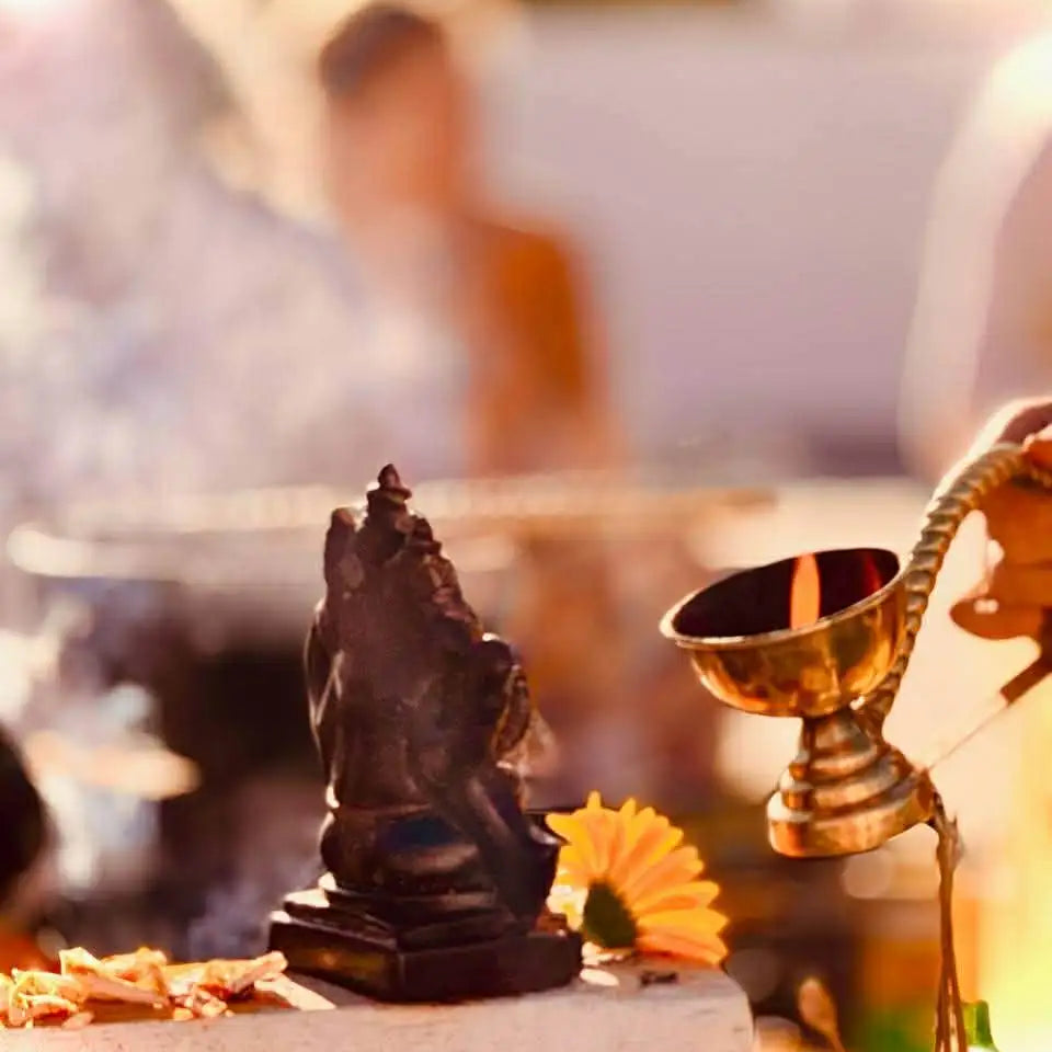 Dark bronze statue of a seated deity with intricate carvings, positioned beside a golden oil lamp.