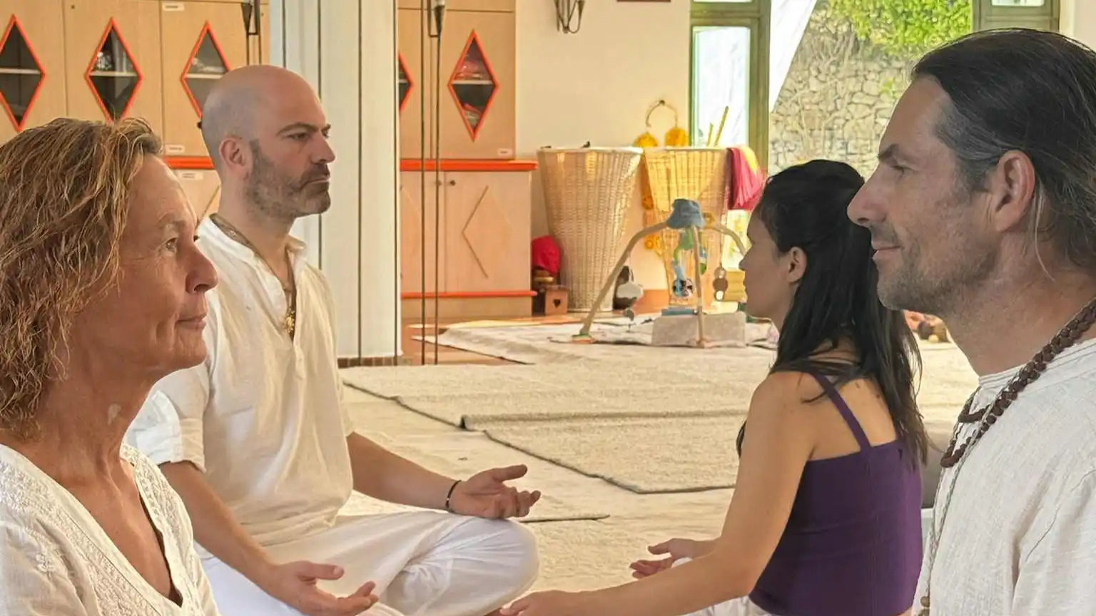 Four people meditating in a bright room.