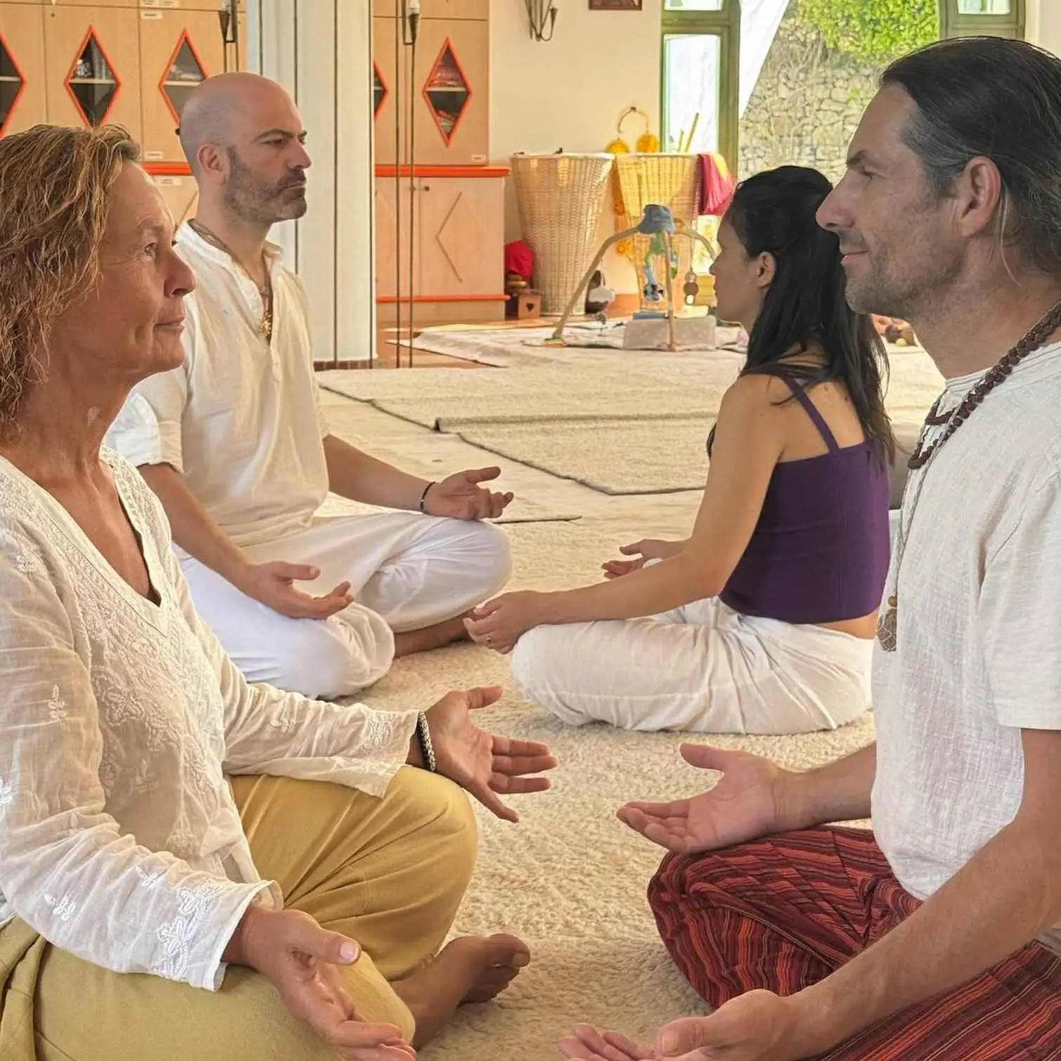 Group of four people in a meditative pose, dressed in loose-fitting white and earth-toned clothing.