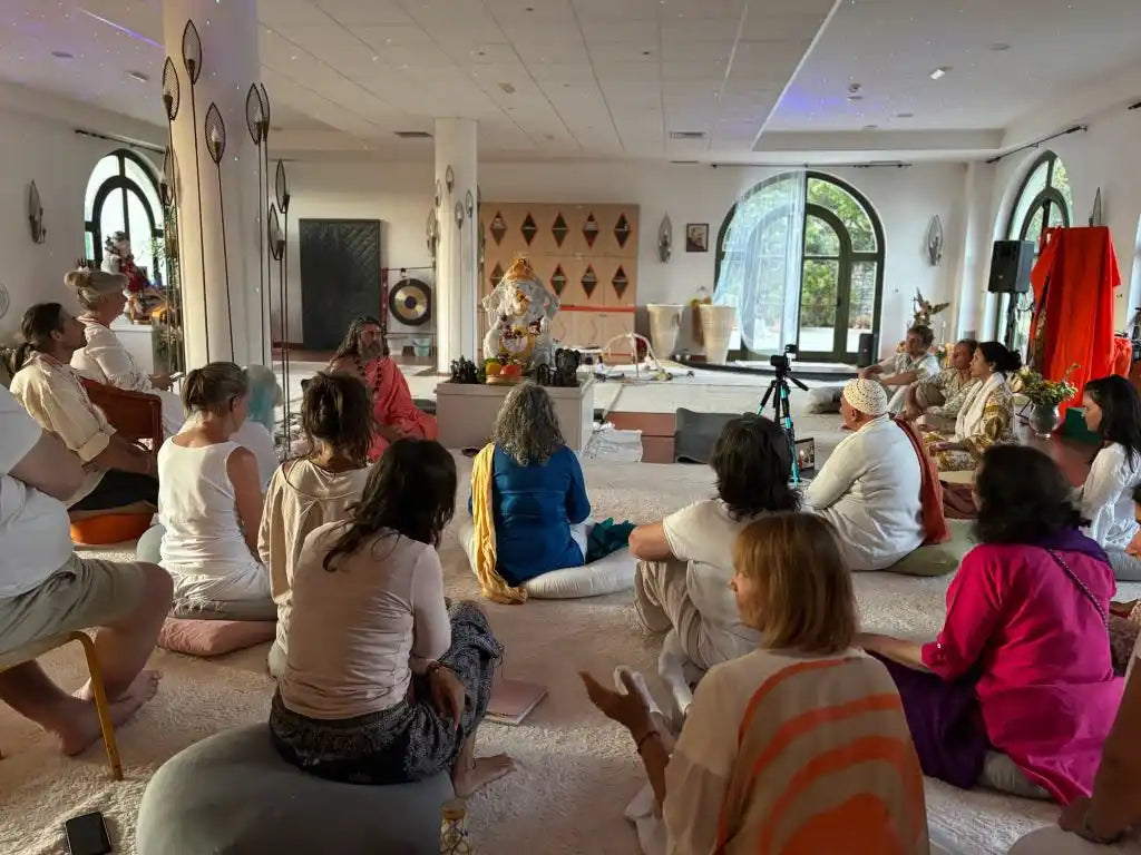A group of people sitting on the floor in a brightly lit room, engaged in what appears to be a spiritual or meditative gathering.