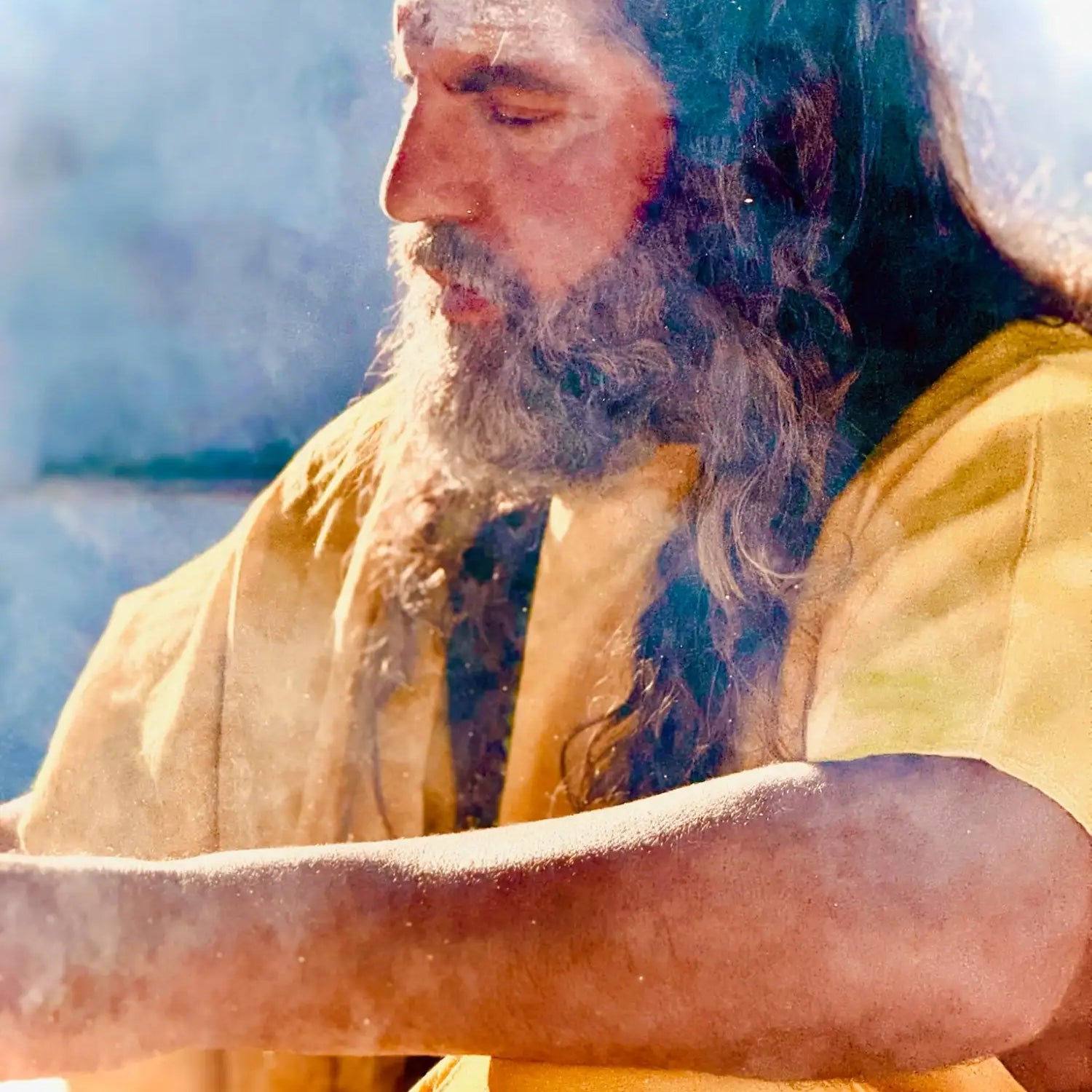 A man with long, dark hair and a full beard wearing a flowing yellow robe.