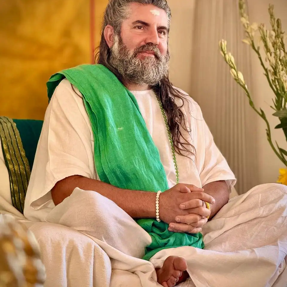 Man with long gray hair and a full beard wearing white robes draped with a vibrant green fabric.