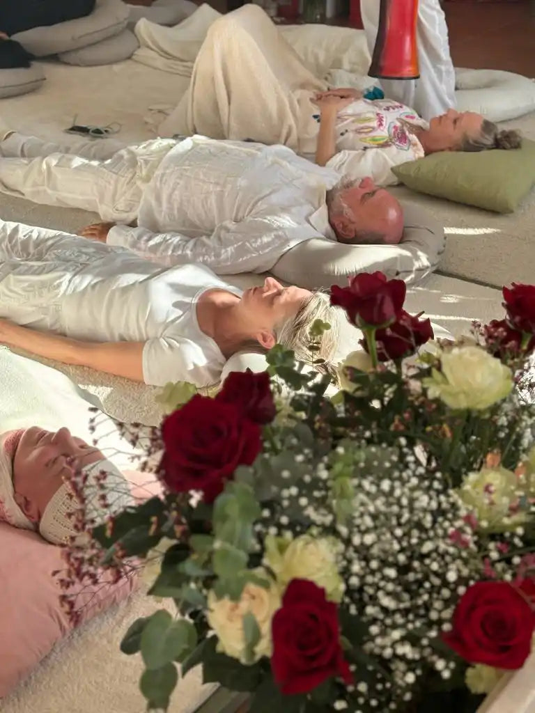 People lying on the floor in white clothing, with a bouquet of red and white roses in the foreground.