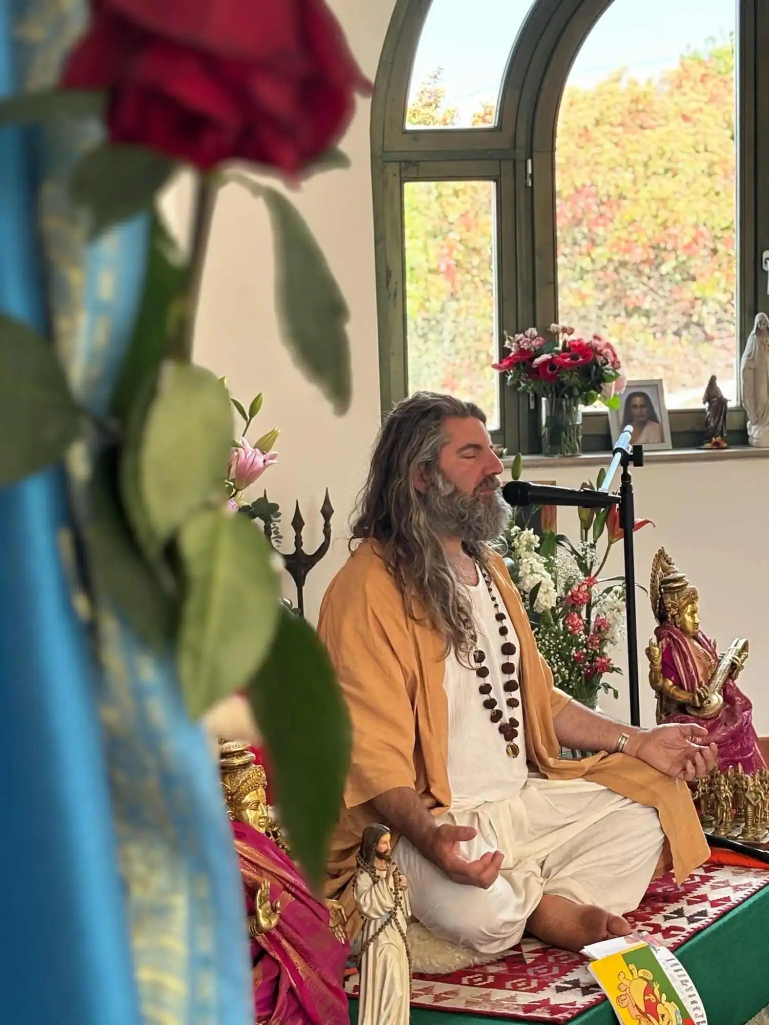 A spiritual teacher with long hair and a beard, meditating in traditional clothing.