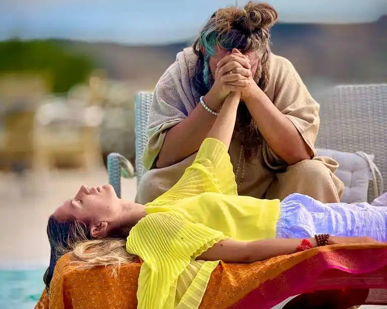 Two individuals engaged in a healing or spiritual practice, with one person lying down and the other holding their hand.