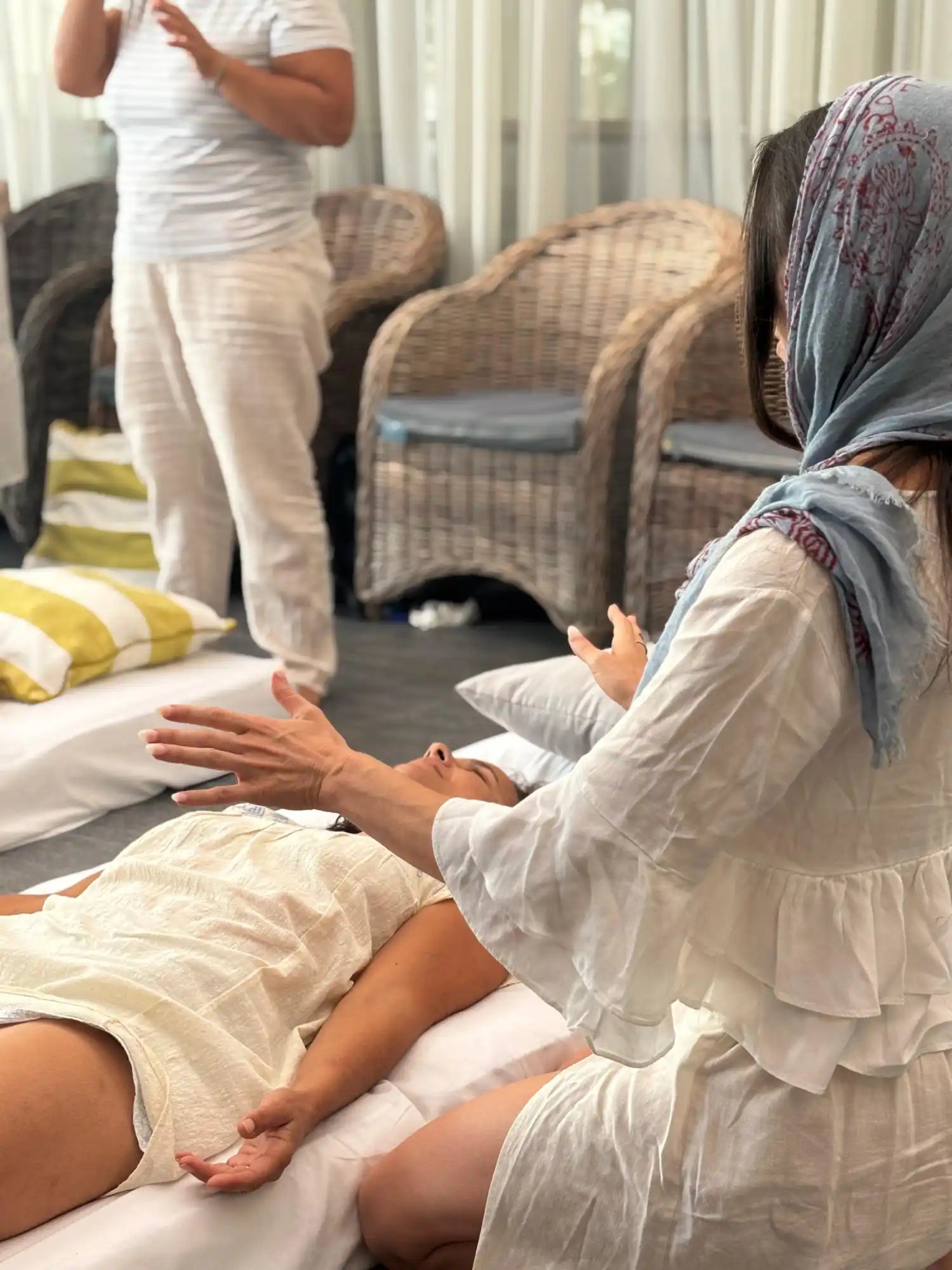 A woman lying on a white cushion, receiving a healing session.